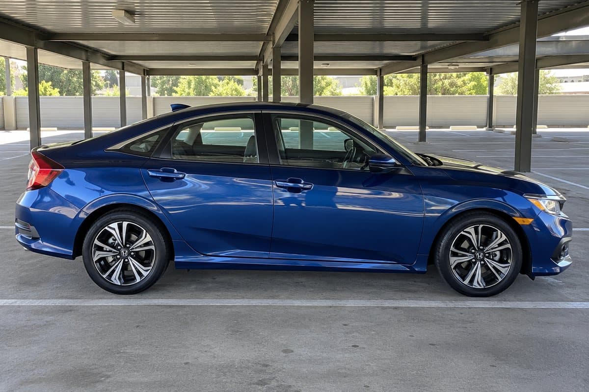 A deep blue metallic Honda Civic under a covered carport, its windows half clear and half tinted