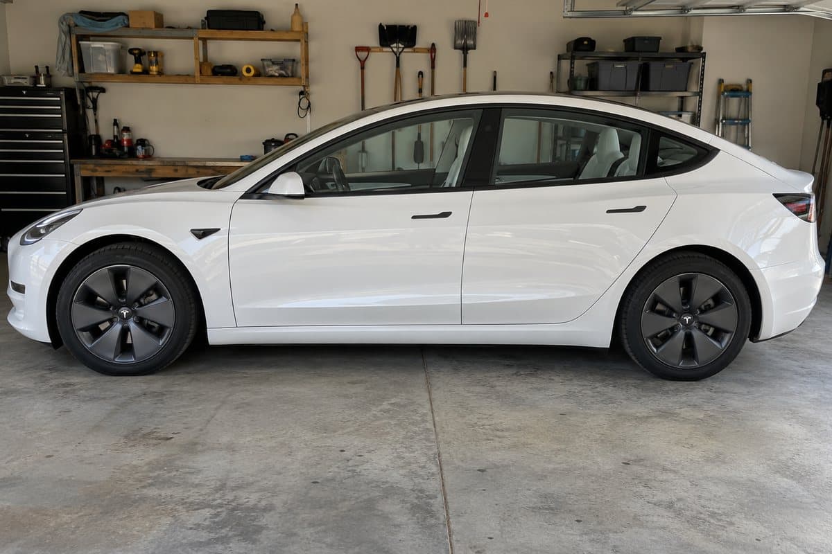 A pearl white Tesla Model 3 in a home garage, its windows half clear and half tinted