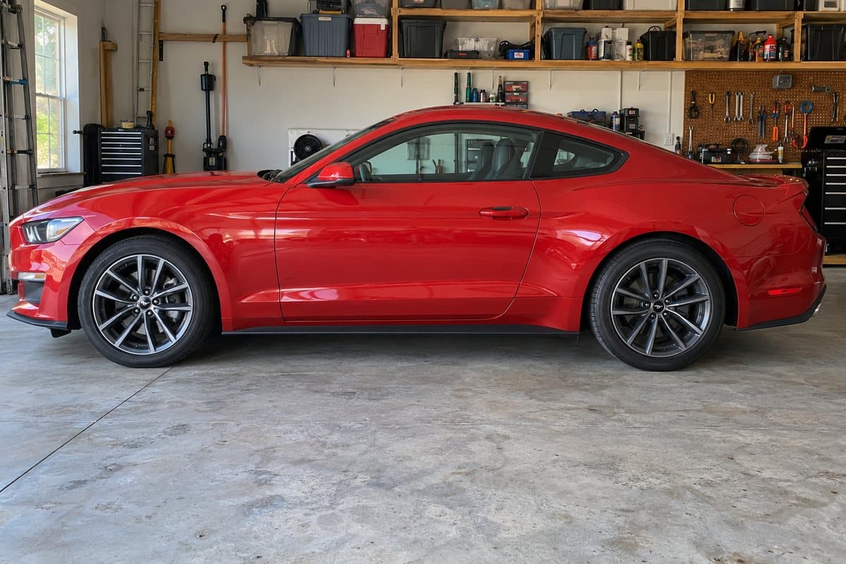 A red Ford Mustang in a home garage, its windows half clear and half tinted