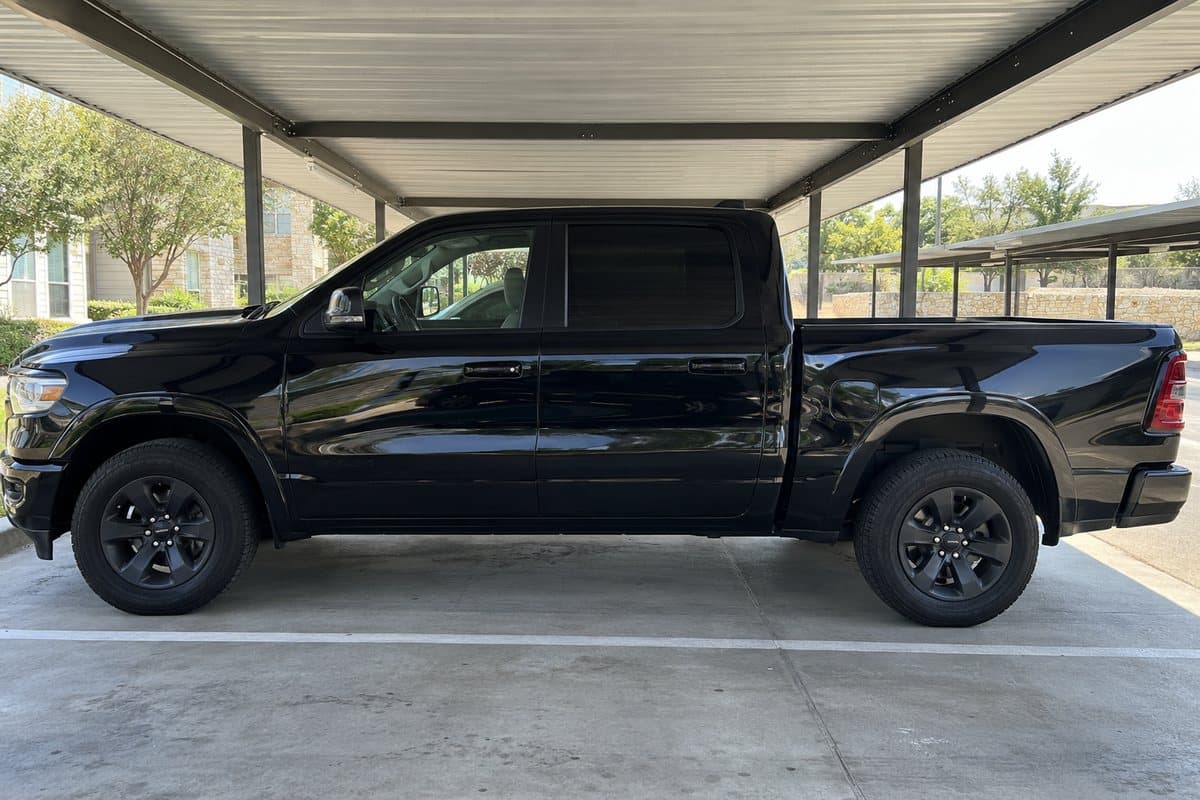 A black Ram 1500 under a covered carport, its windows half clear and half tinted