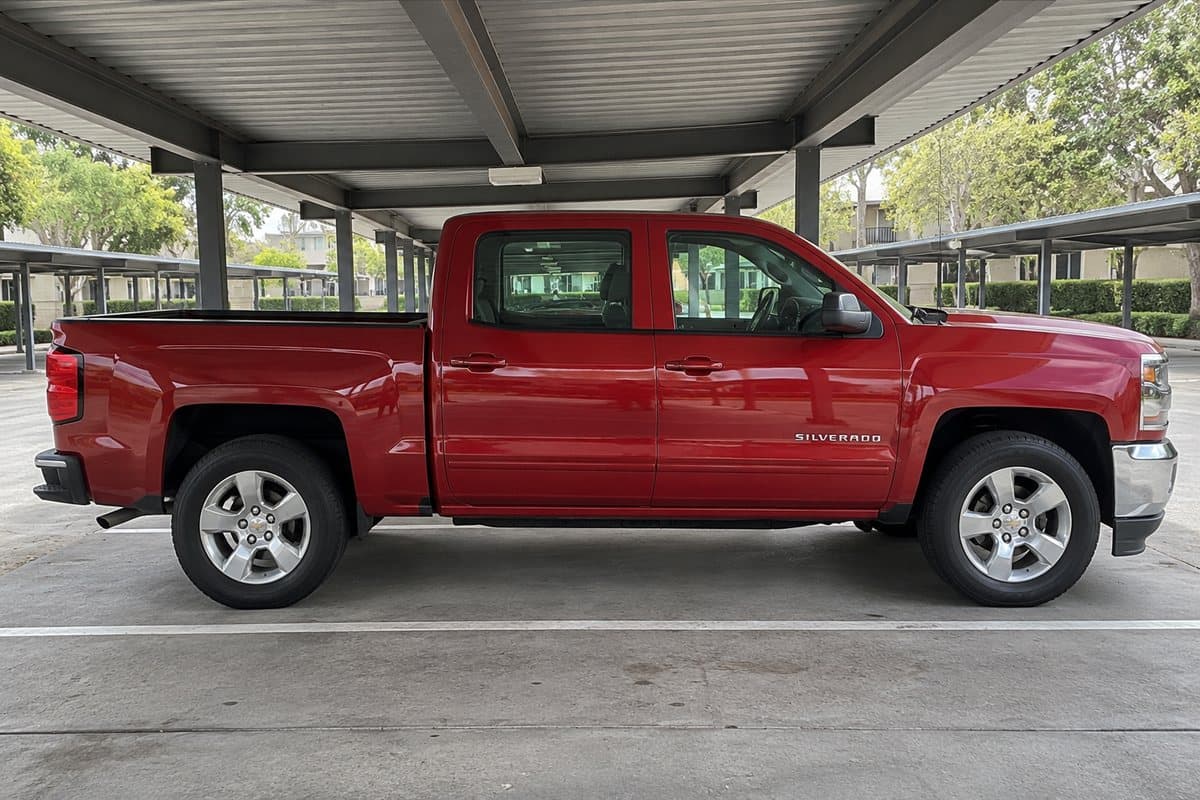 A red Chevy Silverado under a covered carport, its windows half clear and half tinted