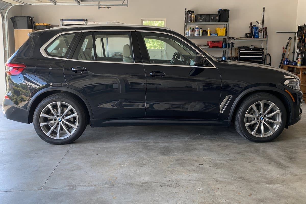 A black sapphire metallic BMW X5 in a home garage, its windows half clear and half tinted