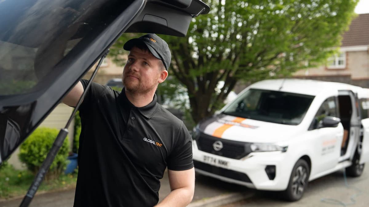 Global Tint installer working beside a vehicle with a branded service van behind him